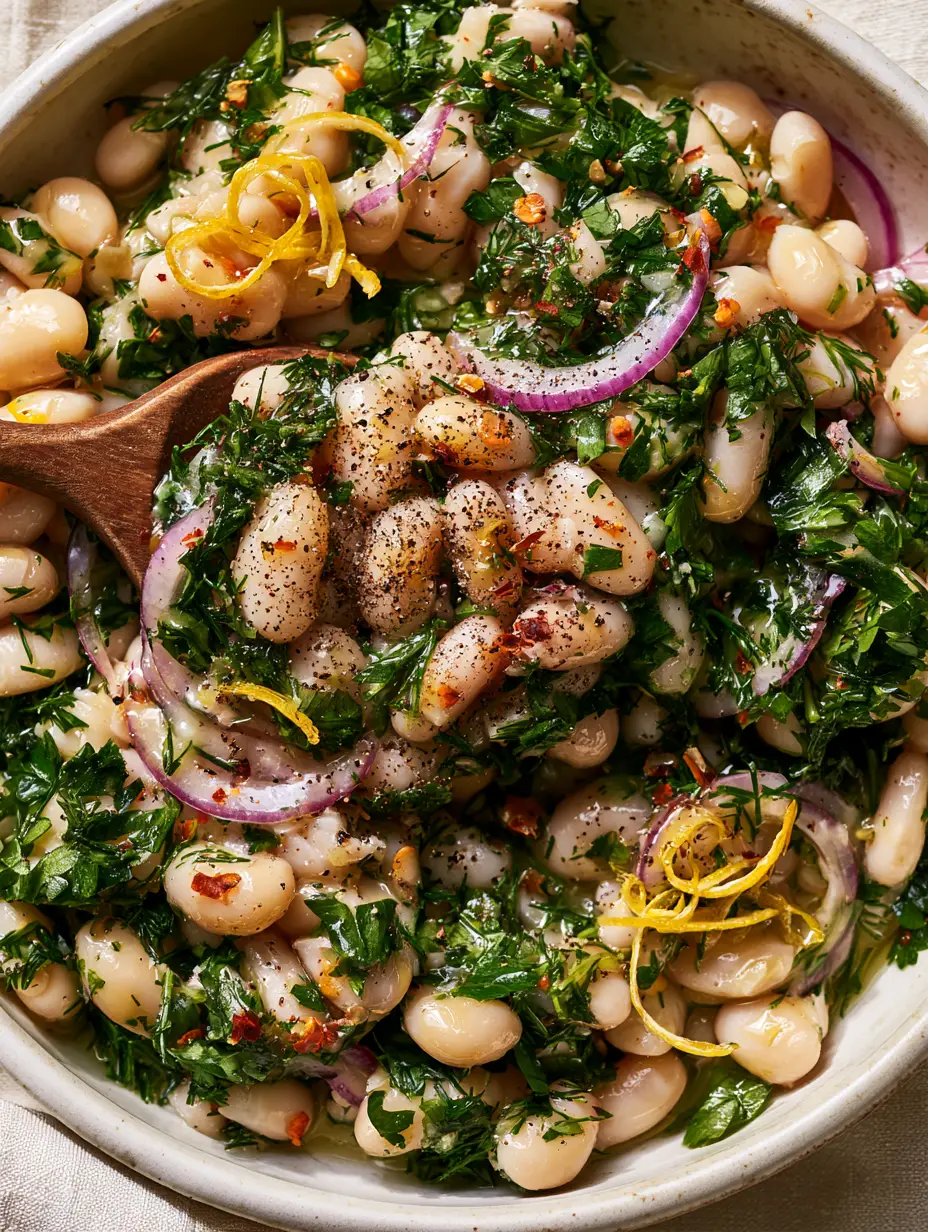 Marinated White Bean Salad with Fresh Herbs and Lemon 3 A close-up shot of glossy cannellini beans in a marinated white bean salad with vibrant green herbs and purple onions.