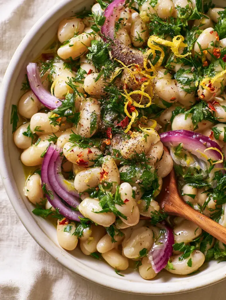 Marinated White Bean Salad with Fresh Herbs and Lemon 1 Marinated white bean salad served in a rustic bowl with a wooden spoon lifting a portion.