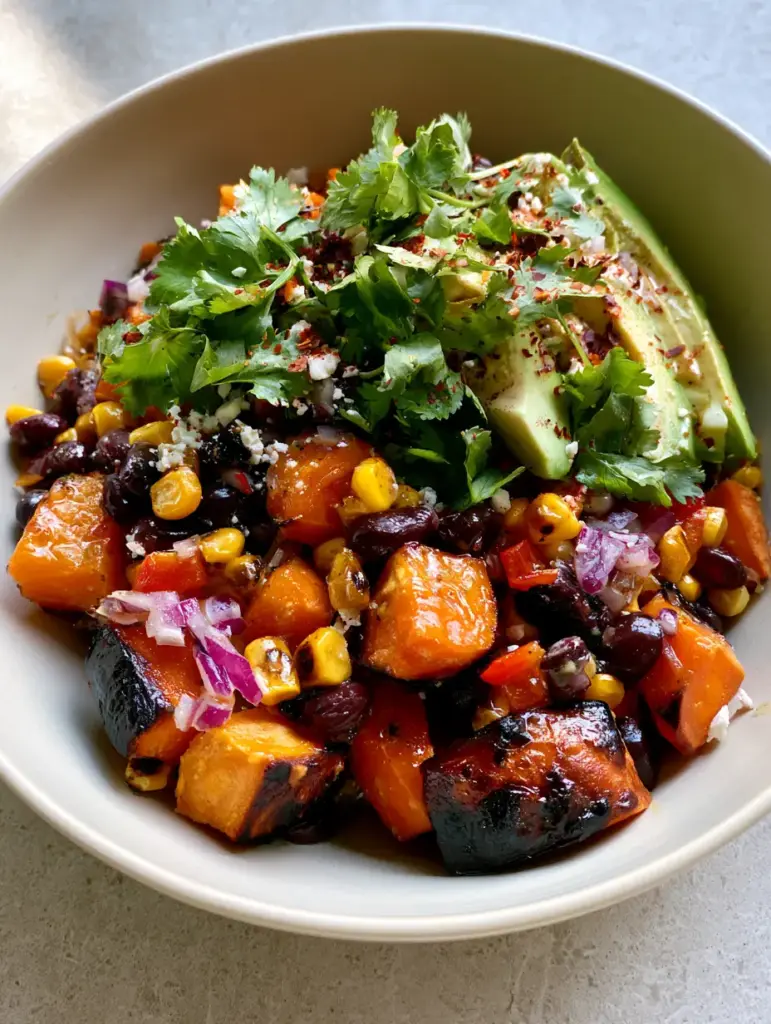Close up shot of fresh cilantro, red bell pepper cubes, and ripe avocado wedges on a black bean salad with sweet potato.