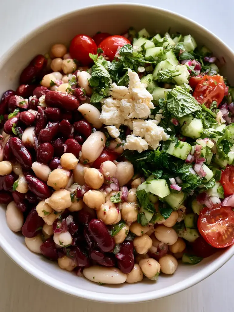 A top-down view of the mixed bean salad in a matte white ceramic bowl on a wood surface.