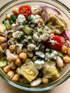 Close up of artichoke dense bean salad showing the fibrous layers of quartered marinated artichokes and glossy vinaigrette.