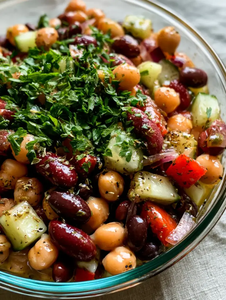 Close-up of red kidney beans and chickpeas coated in glistening lemon-herb vinaigrette in a glass container.