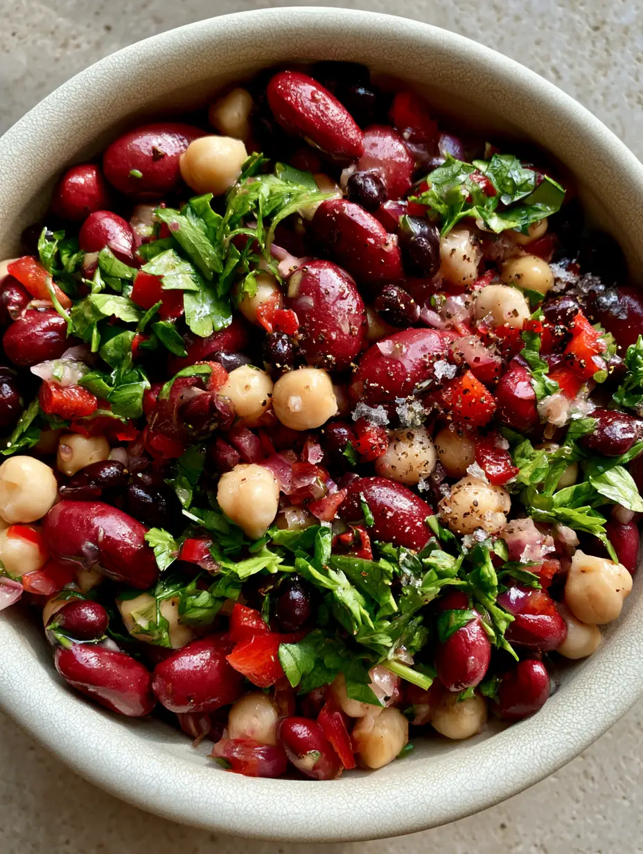 Close-up macro shot of a healthy three bean salad showing the texture of chickpeas, kidney beans, and red peppers with sparkling herb vinaigrette.