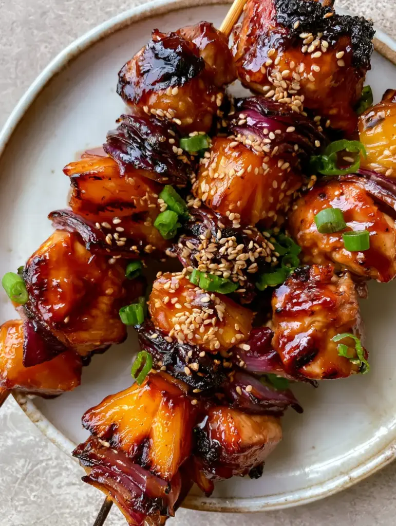 Extreme close-up of charred red onion petals and golden-brown chicken pieces on a kabob. (pineapple chicken kabobs)