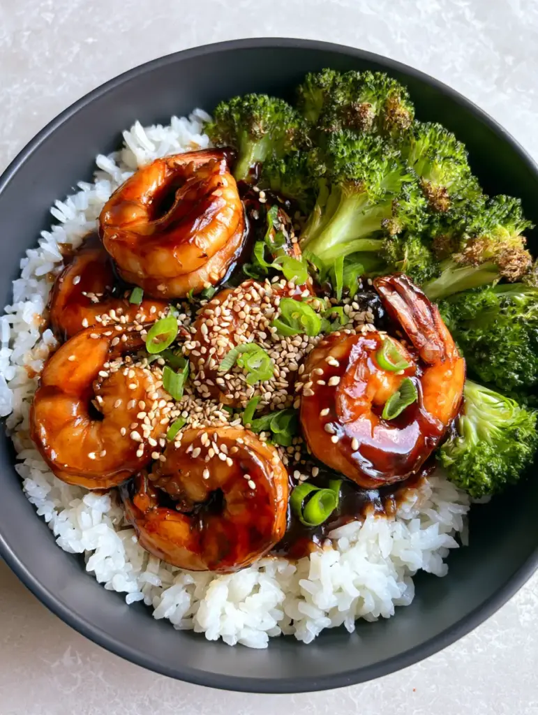 High-angle close-up of blistered bright green broccoli and teriyaki shrimp over white jasmine rice.