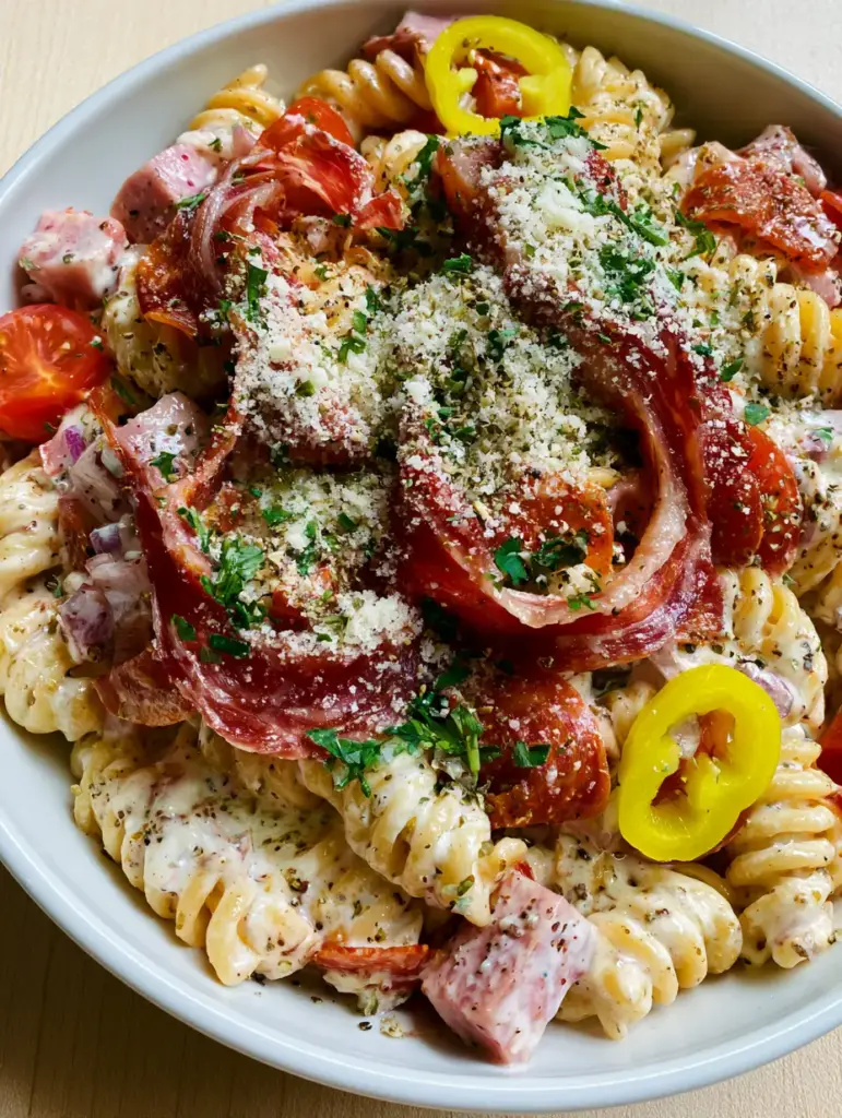 Top-down view of Grinder Pasta Salad garnished with parmesan cheese, parsley, and curled pepperoni. (grinder pasta salad)