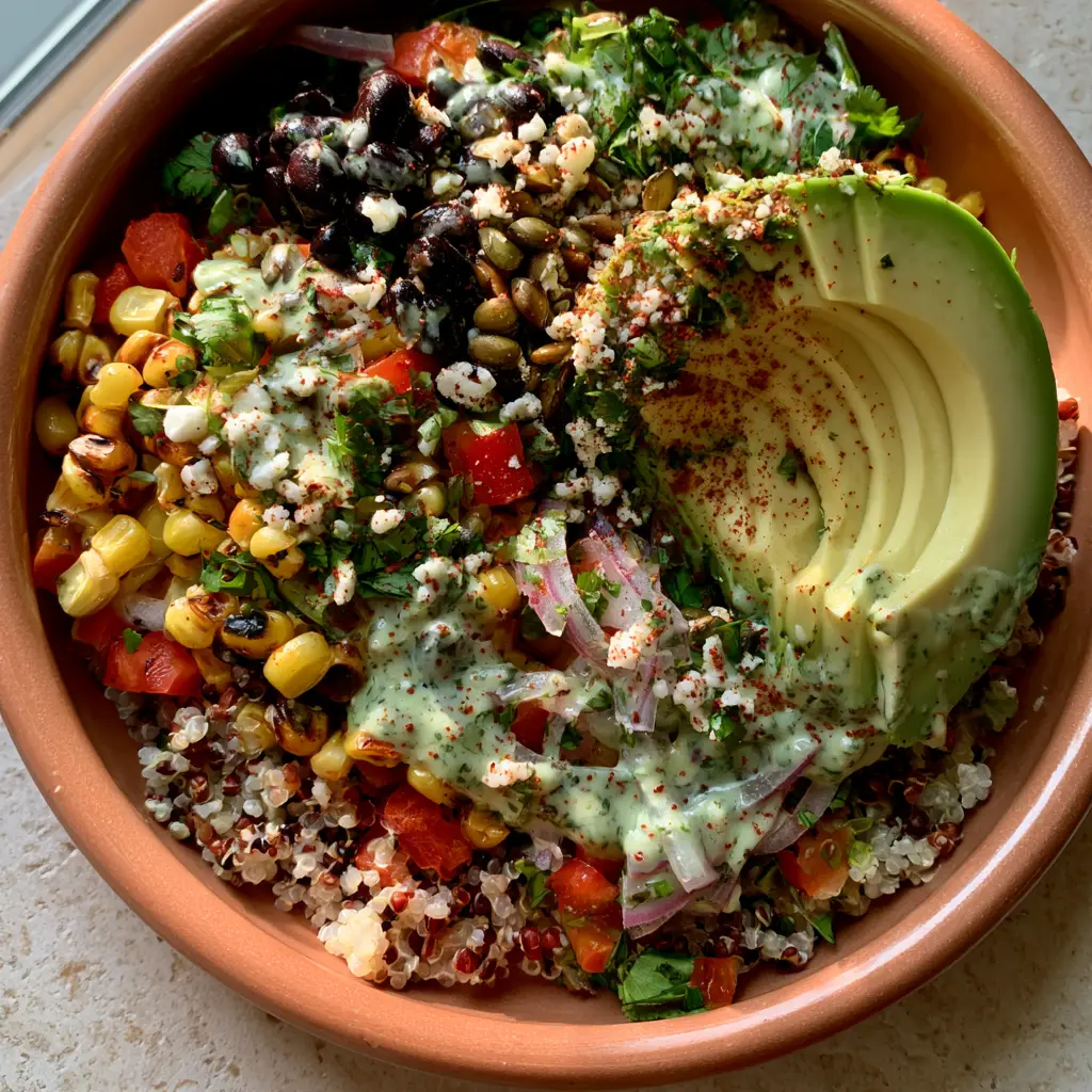 A shallow terracotta bowl showing the finished salade de quinoa mexicaine with a perfectly sliced avocado fan and toasted pepitas.