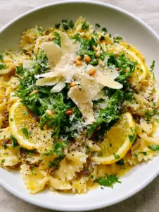 Top-down 45-degree angle shot of Lemon Dijon Pasta Salad featuring farfalle ribbons and visible mustard seeds in a matte white ceramic bowl.